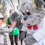 Costumed character greets child in outdoor setting as others look on