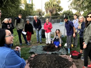 Adults grouped around pile of dirt in a park