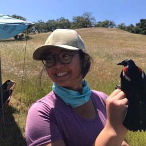 Photo of smiling woman in hat and glasses handling bird. 