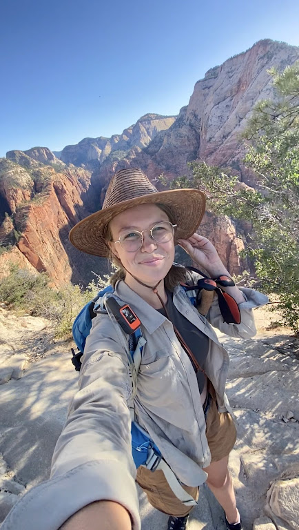 Woman in glasses and hat posing for a selfie with a desert canyon in the background.
