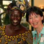 Two women smile at the camera. One is wearing traditional African clothing.