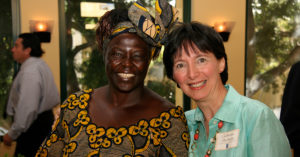 Two women smile at the camera. One is wearing traditional African clothing.