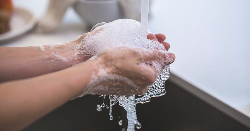 hands lathered with soap bubbles under running water in sink